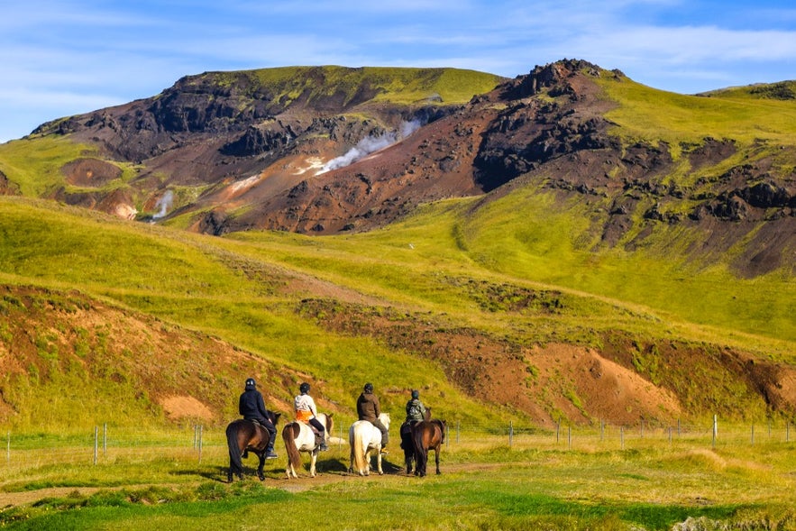Riders on Icelandic horses explore green volcanic hills in Iceland in June under clear summer skies.