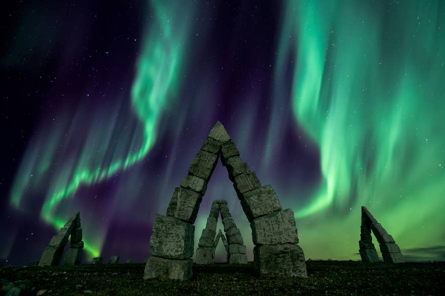 Zorza polarna świeci nad kamiennymi rzeźbami Arctic Henge w Raufarhofn na Islandii nocą.