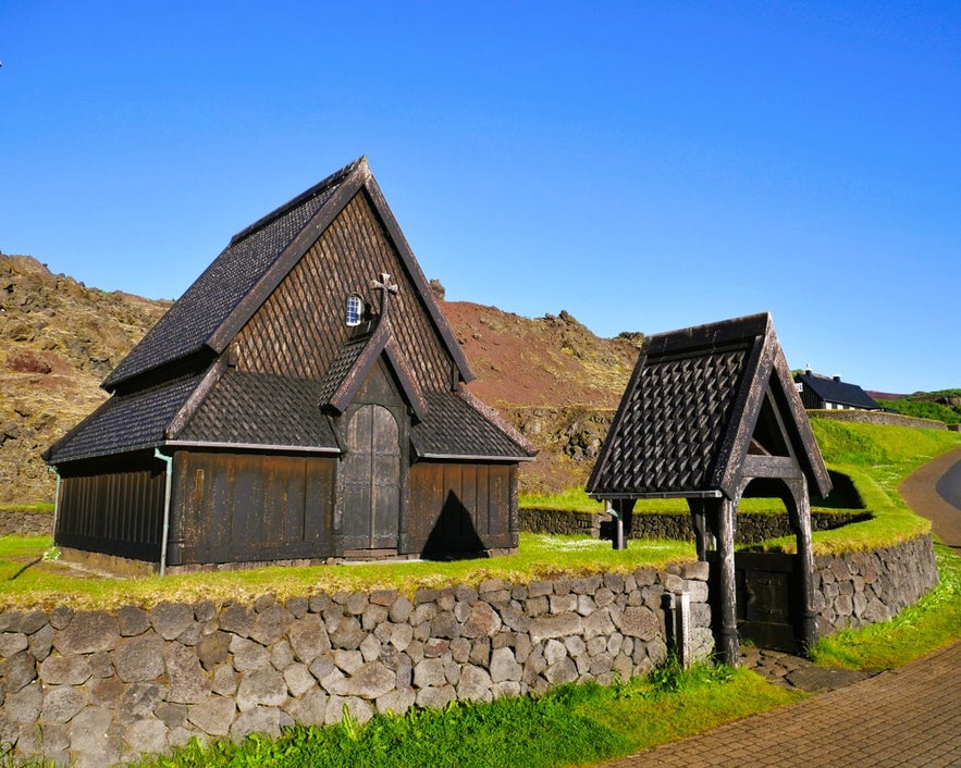 Heimaey Stave Church with turf walls and lava rock backdrop under clear skies in South Iceland.