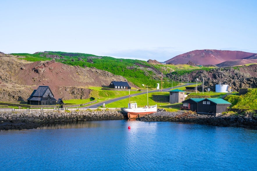 Scenic harbor view of Heimaey with Stave Church, fishing boat, and Eldfell Volcano in South Iceland.