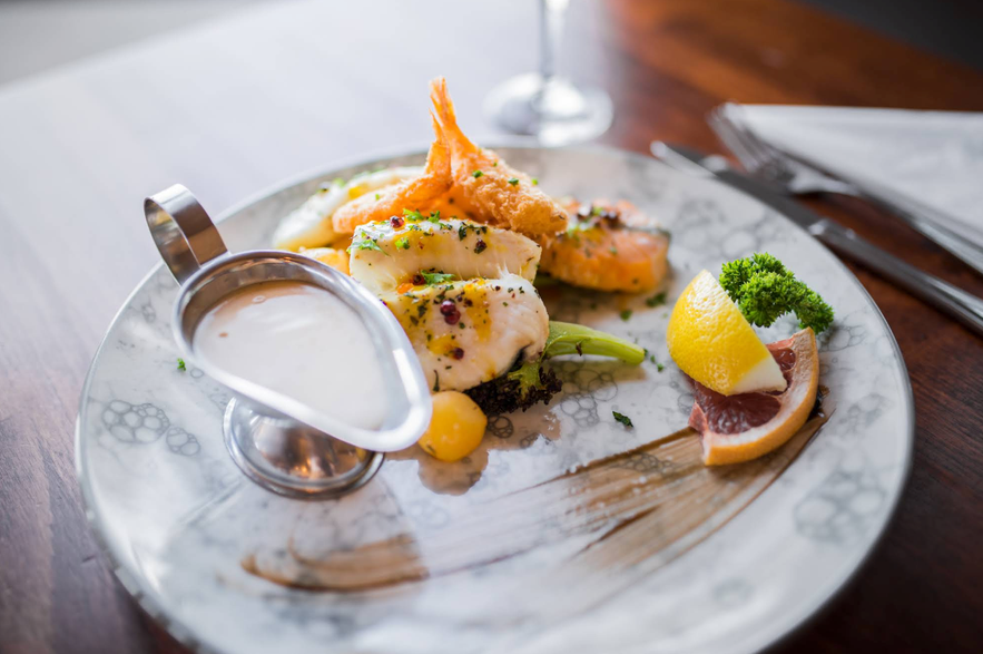 Plated seafood dish at Kaffi Duus in Keflavik, featuring grilled white fish, salmon, fried shrimp, fresh garnish, lemon wedge, and creamy sauce served on a marble-patterned plate.