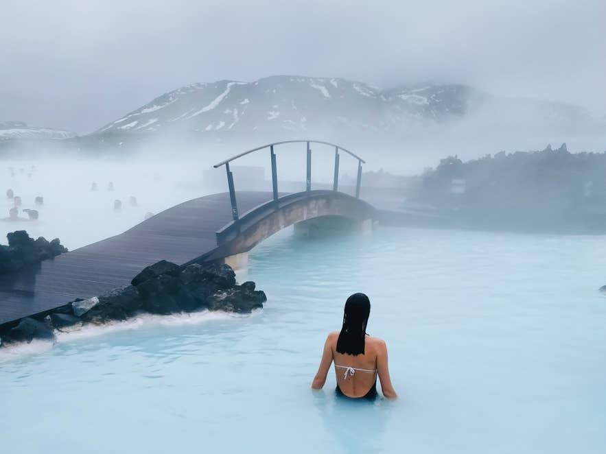 ブルーラグーンの温泉でリラックスする女性。蒸気と火山風景に囲まれたアイスランドの絶景スパ。