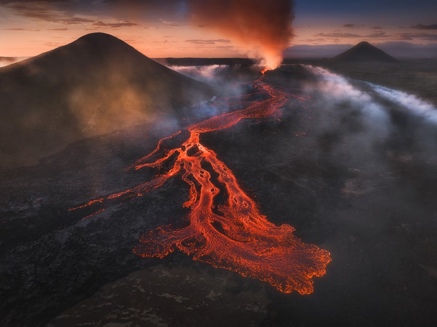 Aerial view of Litli-Hrutur volcanic eruption near Fagradalsfjall in Iceland with glowing lava flow and smoke at sunset.