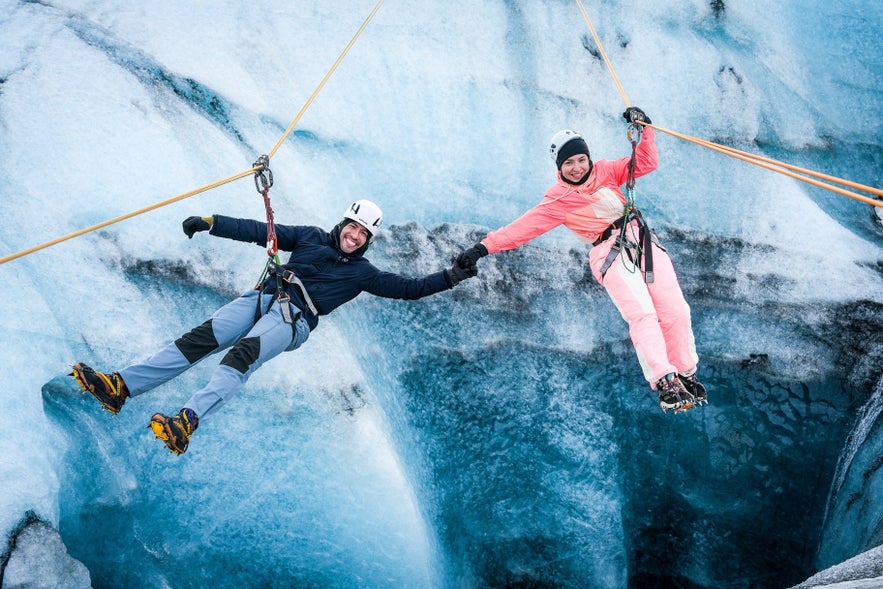 Couple ziplining over Solheimajokull glacier in Iceland with safety gear and smiling faces.