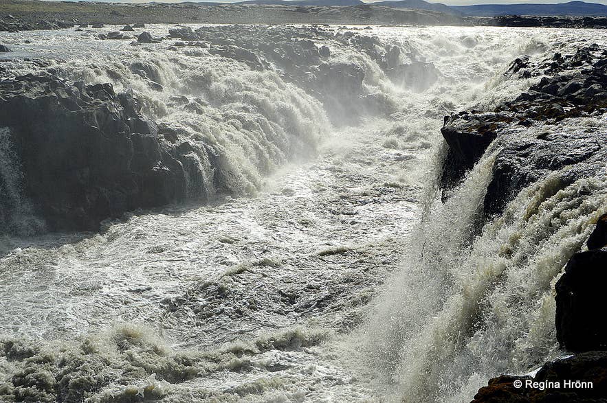 Grey glacial water of Jökulsá á Fjöllum pouring over dark rock ledges into the gorge at Gljúfrasmiður