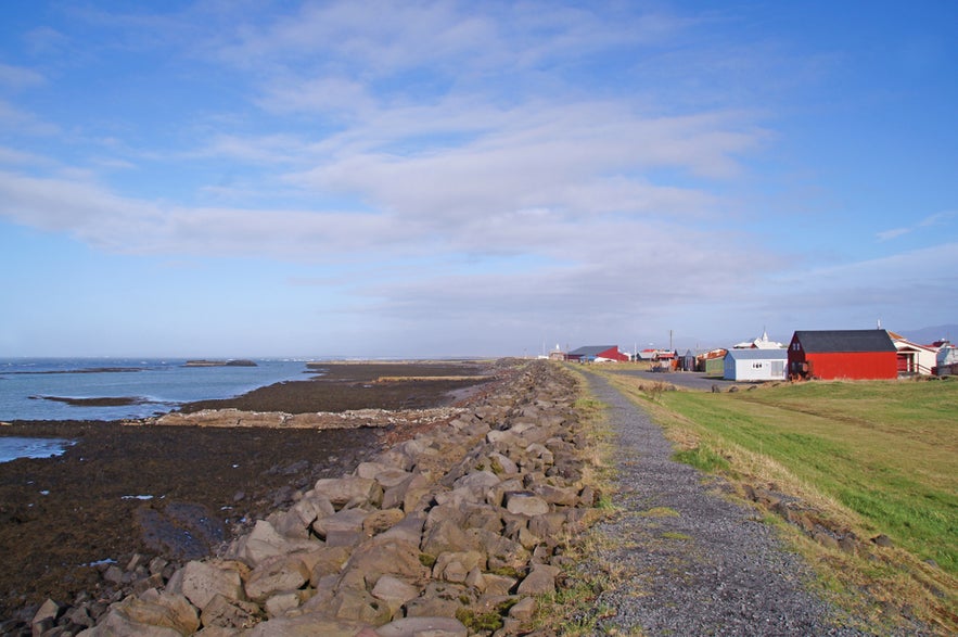 Coastal path along the rocky shore by the colorful houses of Eyrarbakki village, Iceland, on a clear sunny day.