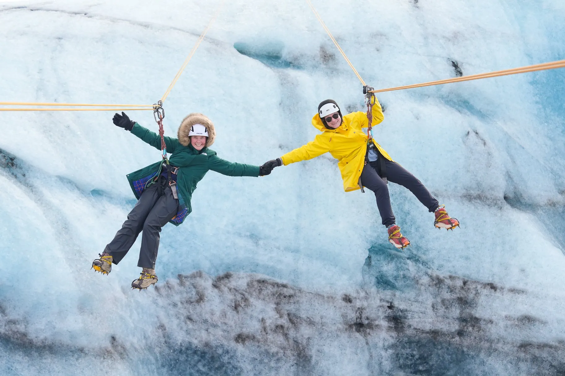 Deux voyageurs se tenant joyeusement la main alors qu'ils sont suspendus dans les airs lors d'une randonnée sur glacier et d'une descente en tyrolienne à Solheimajokull.