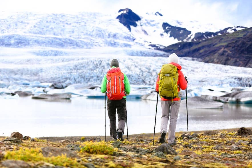 Dwoje turystów wędrujących w pobliżu lodowca Vatnajokull z kijkami trekkingowymi i plecakami, ubranych warstwowo i wyposażonych na wycieczki po Islandii w chłodną pogodę.