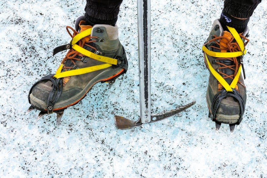 Close-up of crampon-fitted hiking boots and ice axe on glacier, showing essential clothes and gear for Iceland tours.