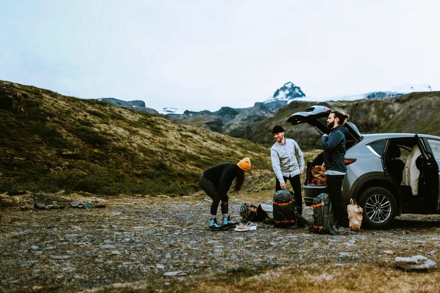 Travelers unpacking clothes and gear for Iceland tours from a car in the countryside, preparing for outdoor adventure.
