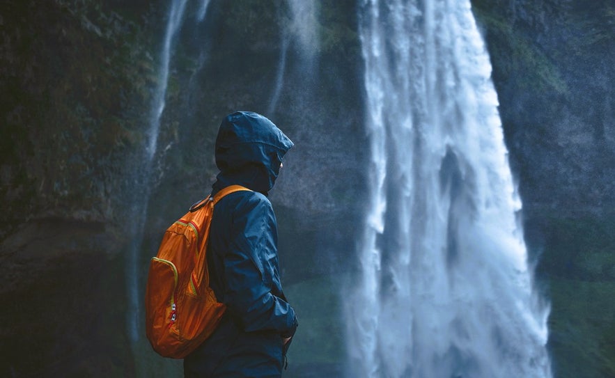 Traveler at Seljalandsfoss Waterfall showing what to wear in Iceland for rainy, windy days on the South Coast.