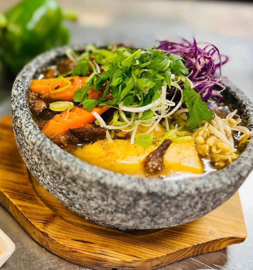 Stone bowl of vegan bon bu hue, with carrots, sprouts, and herbs, at Vegan World Peace, a vegan restaurant in Reykjavik.