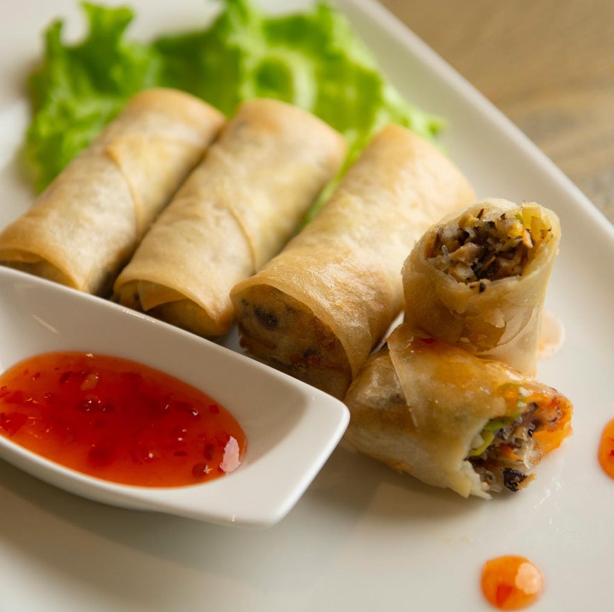 Spring rolls with lettuce and red dipping sauce served at Loving Hut on a white plate.