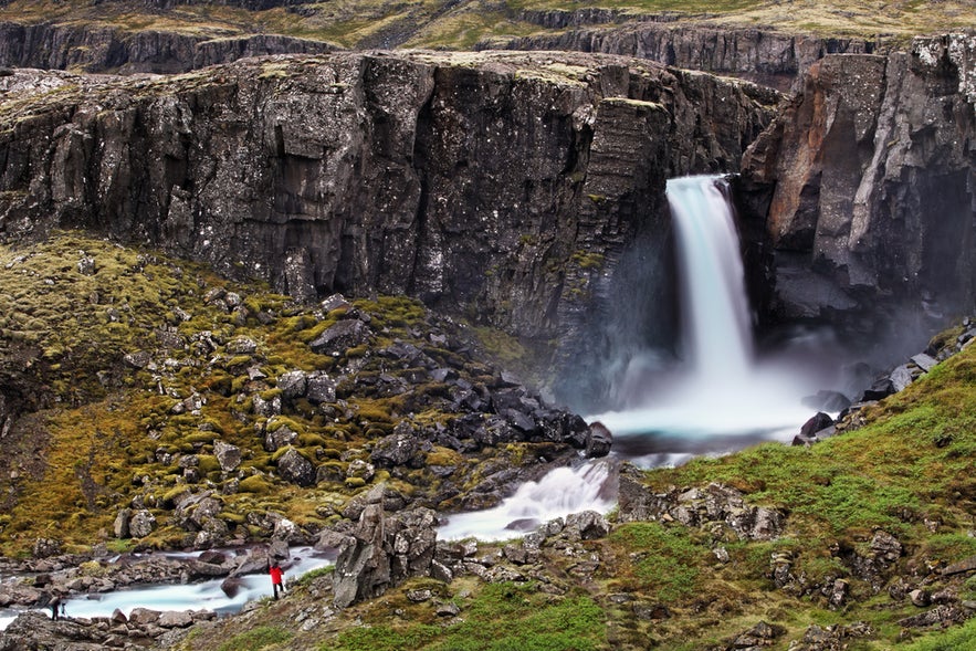 Bleiksarfoss waterfall cascading into a rocky, moss-covered gorge in Eskifjordur, East Iceland.