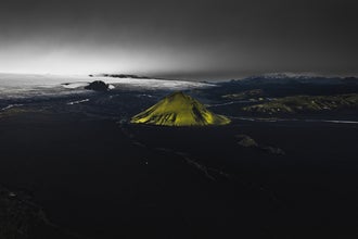 The Maelifell volcano looms in the distance, its bright green color contrasting with the surrounding black-sand landscape.