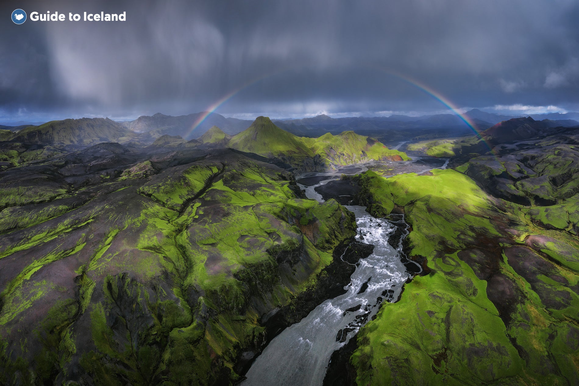 A river canyon and green mountains in the Icelandic Highlands with a rainbow above.