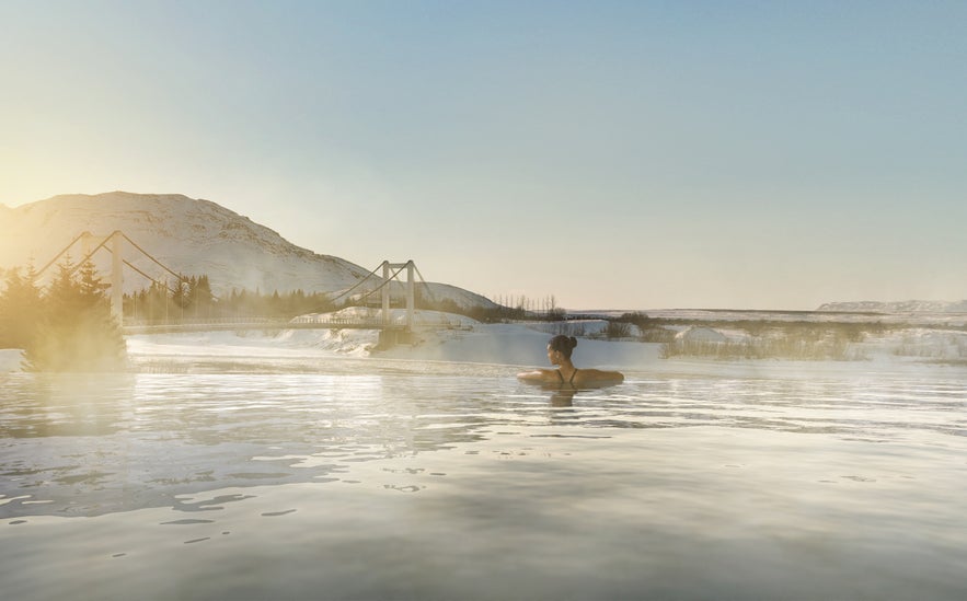 Woman bathing in Laugaras Lagoon with views of the Hvita River and South Iceland’s countryside.
