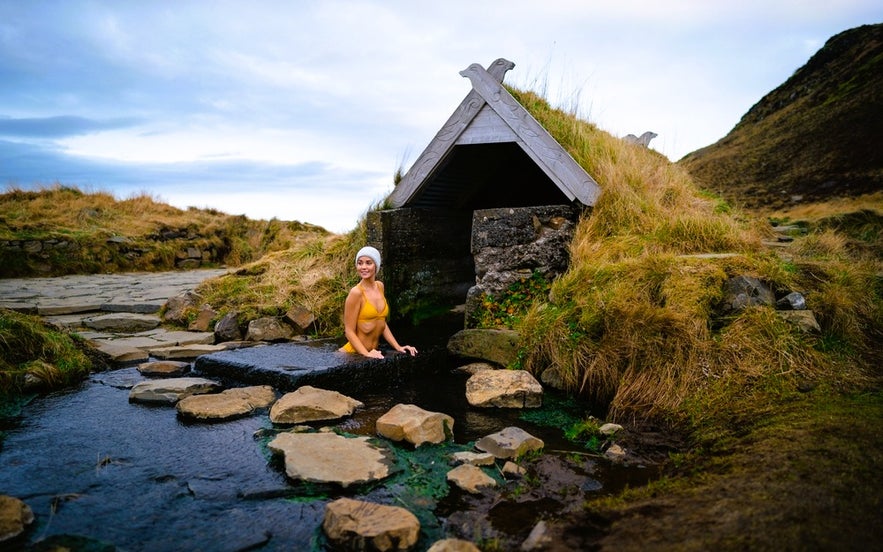 Traveler in a hot spring at Reykjadalur Valley shows what to wear in Iceland for geothermal bathing in natural pools.