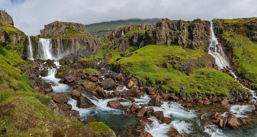 Twin waterfalls cascade over Bjolfur mountain’s green slopes in Seydisfjordur, Iceland on a summer Vestdalsfossar hike.