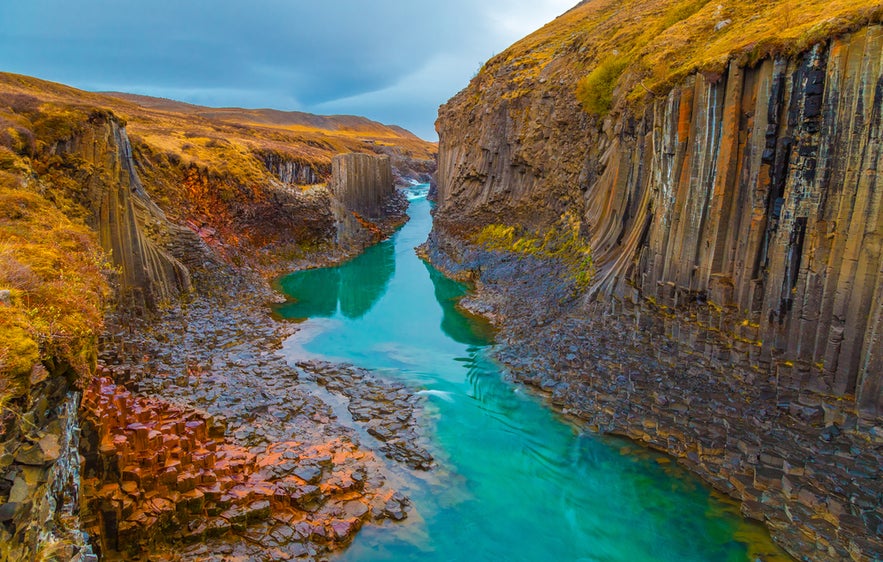 Studlagil Canyon in East Iceland, featuring turquoise water and striking basalt columns on both sides of the river.