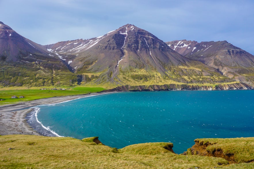 Borgarfjordur Eystri in East Iceland, featuring a turquoise bay, black sand beach, and dramatic snow-capped mountains.