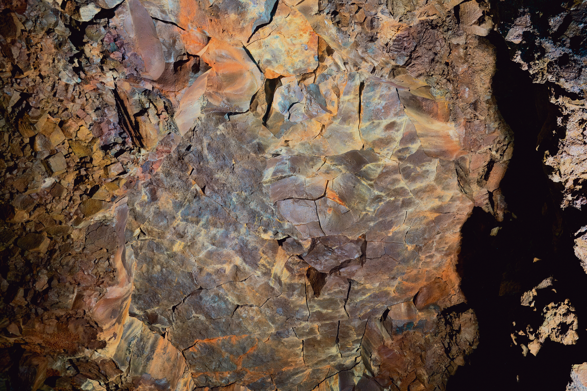 Orange, blue, and brown hues color the cracked rock walls inside Vidgelmir Cave in West Iceland.