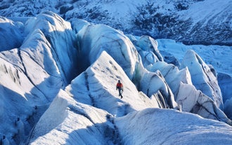 A man hikes over large ice formations on a glacier during a South Coast tour in Iceland.