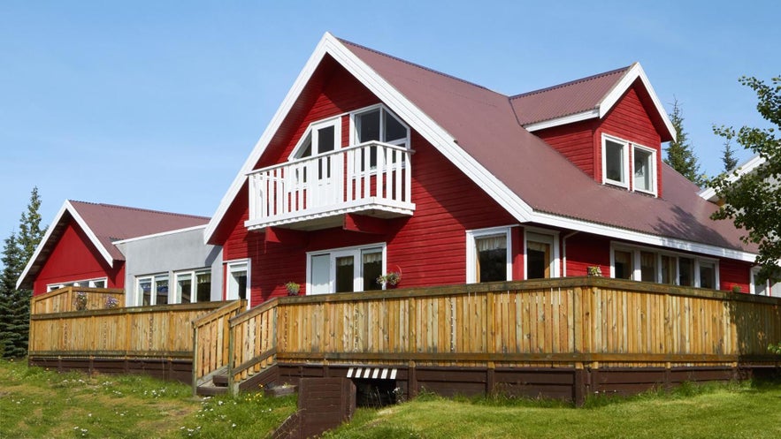 Hotel Eyvindara in East Iceland, featuring a red wooden building with a balcony and fenced terrace surrounded by greenery.