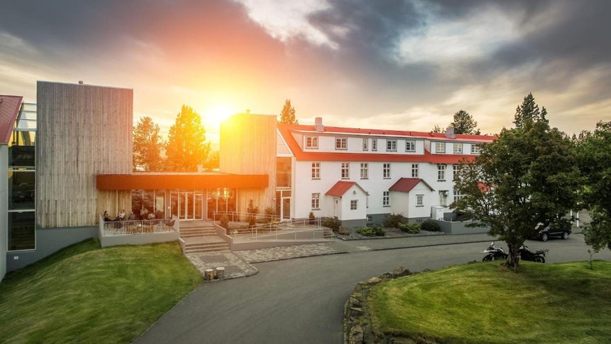 Gistihusid Lake Hotel Egilsstadir at sunset, featuring modern and traditional architecture in a green, scenic setting.