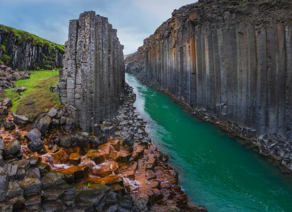 Vue éclatante du canyon de Studlagil dans l'est de l'Islande, avec une rivière glaciaire turquoise serpentant entre des colonnes de basalte saisissantes et des roches colorées par les minéraux.