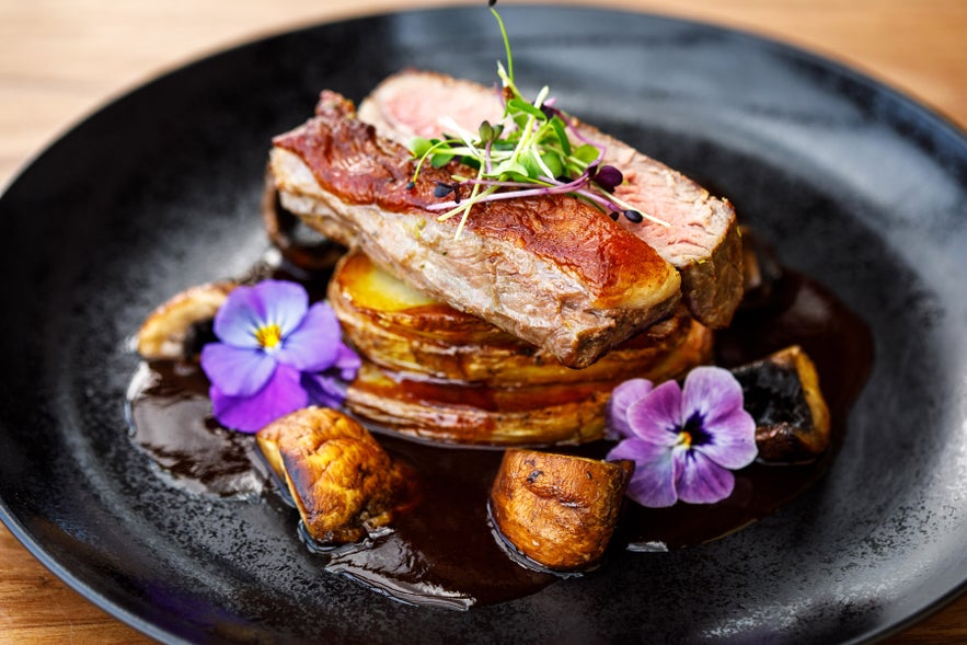 Lamb dish with roasted potatoes, mushrooms, and edible flowers at the South Iceland restaurant, Systrakaffi.