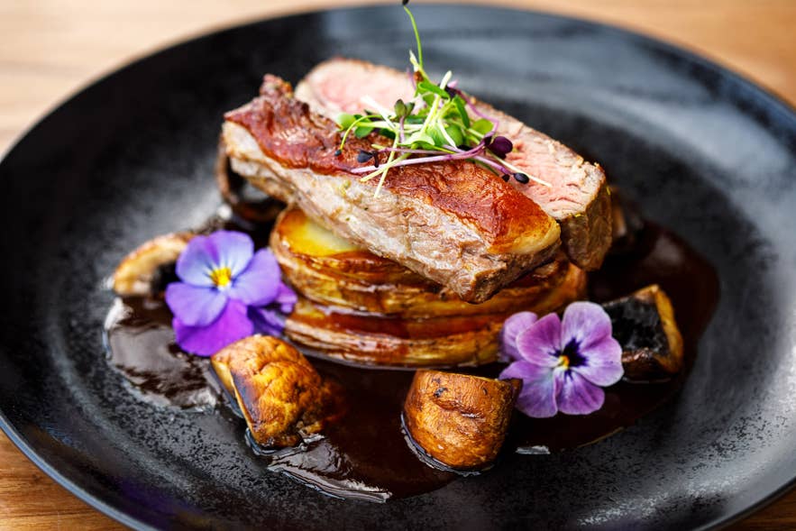 Lamb dish with roasted potatoes, mushrooms, and edible flowers at the South Iceland restaurant, Systrakaffi.