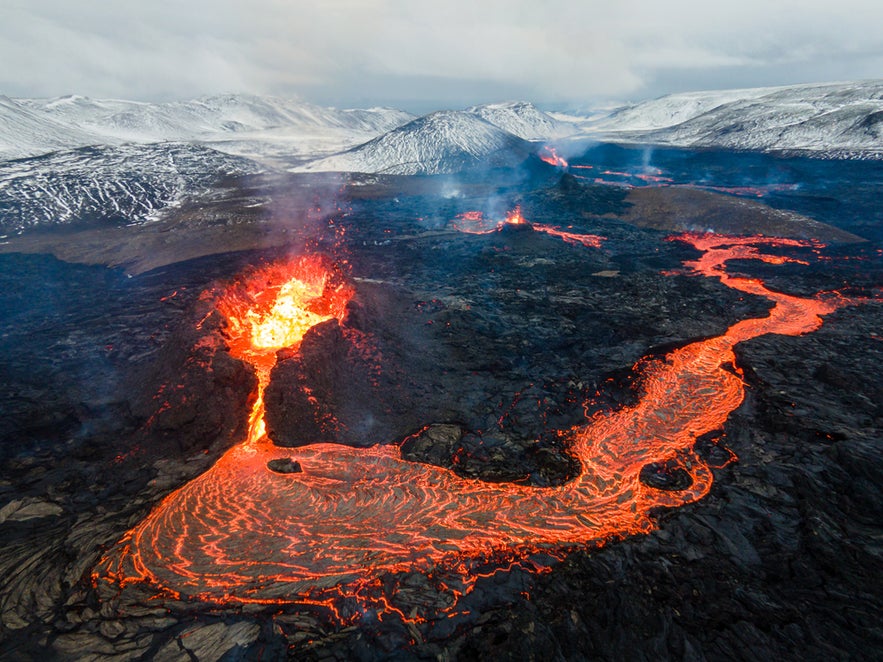 Fagradalsfjall Volcano erupting, glowing lava flowing—first stage of Iceland’s volcanic way, snowy peaks in the distance. Fagradalsfjall Volcano erupting, glowing lava flowing—first stage of Iceland’s volcanic way, snowy peaks in the distance.