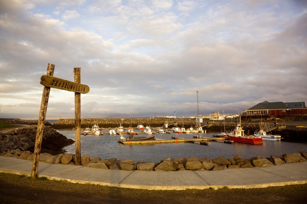 Boats docked at Keflavík Marina in Iceland during golden hour, with a wooden sign reading “Skessuhellir” in the foreground.