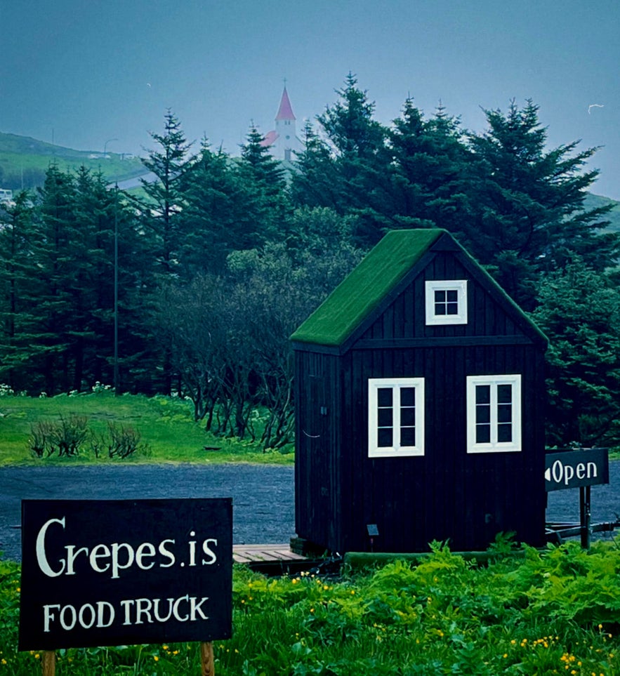 Crepes.is food truck in South Iceland, housed in a small black hut with a grass roof, surrounded by trees and countryside.