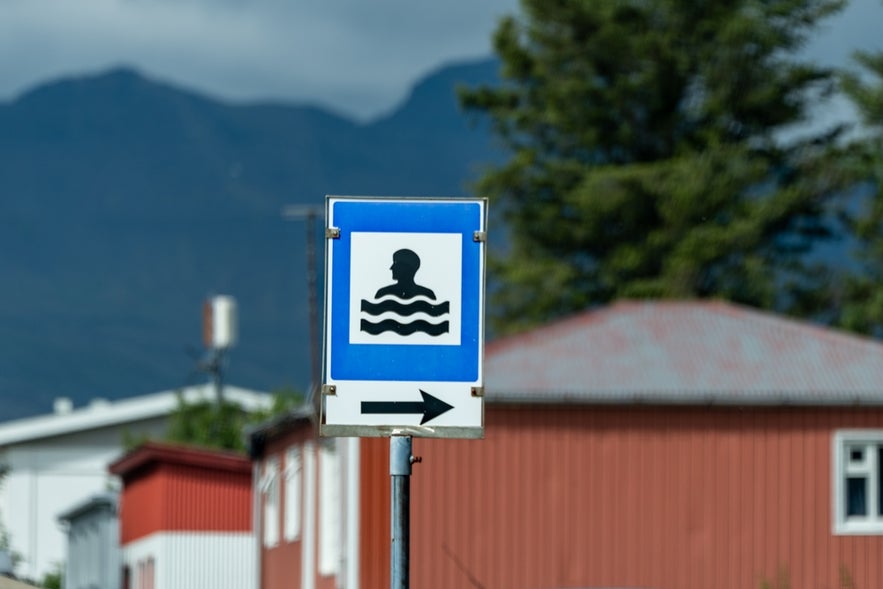 A blue and white square service sign with a black image of a person in water indicates the presence of a swimming pool.