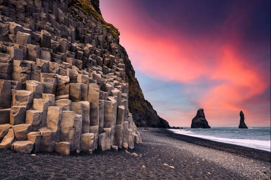 Basalt columns and sea stacks at Reynisfjara Beach, Iceland, illuminated by the colorful glow of the midnight sun.