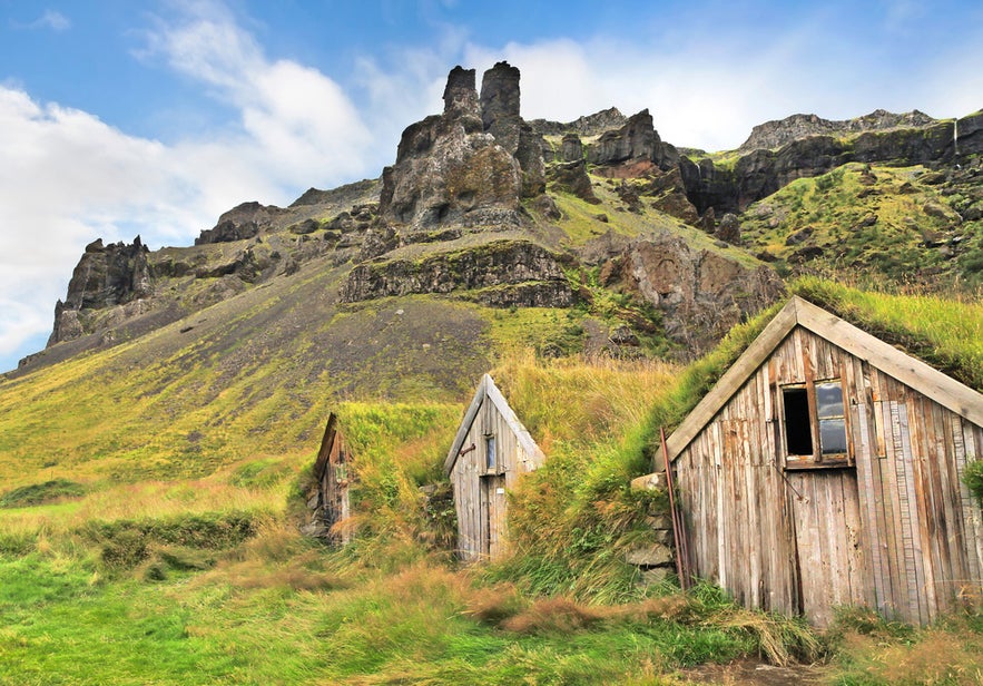 Traditional turf houses at Nupsstadur farm near Skaftafell, set against rocky cliffs and lush green slopes.