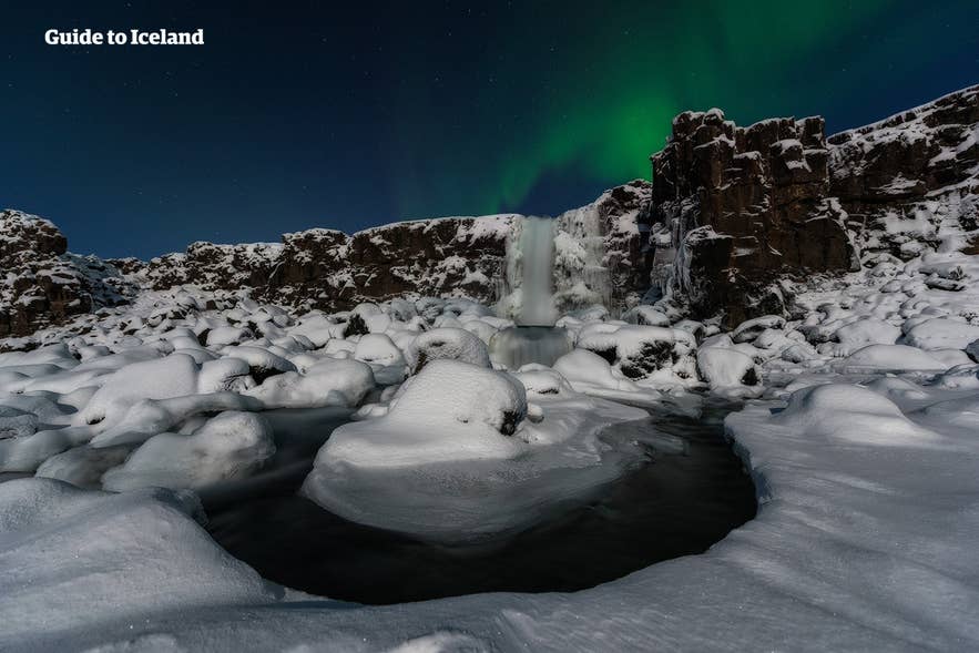 La cascata Oxararfoss coperta di neve sotto l'aurora boreale nel Parco Nazionale di Thingvellir in inverno.