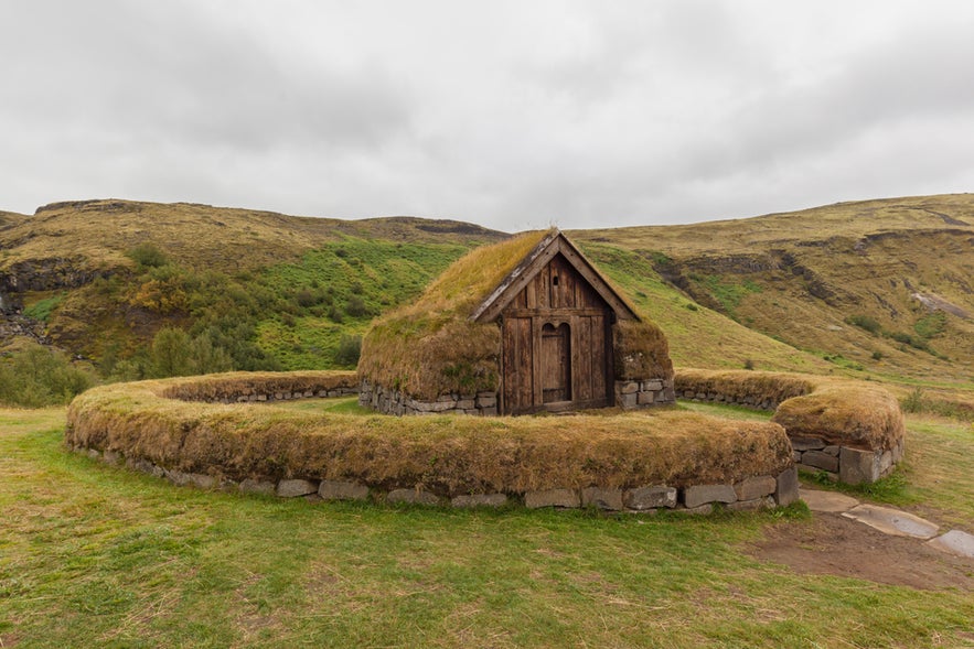 Turf house at Thjodveldisbaerinn Strong, set in a grassy Icelandic valley under cloudy skies.