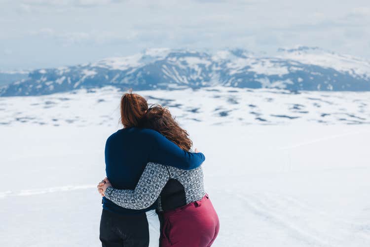 Two female visitors on a midnight sun tour to Langjokull Glacier in Iceland hug as they admire the surrounding frozen landscape.