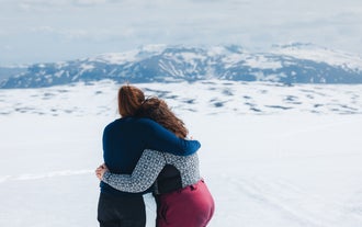 Two female visitors on a midnight sun tour to Langjokull Glacier in Iceland hug as they admire the surrounding frozen landscape.