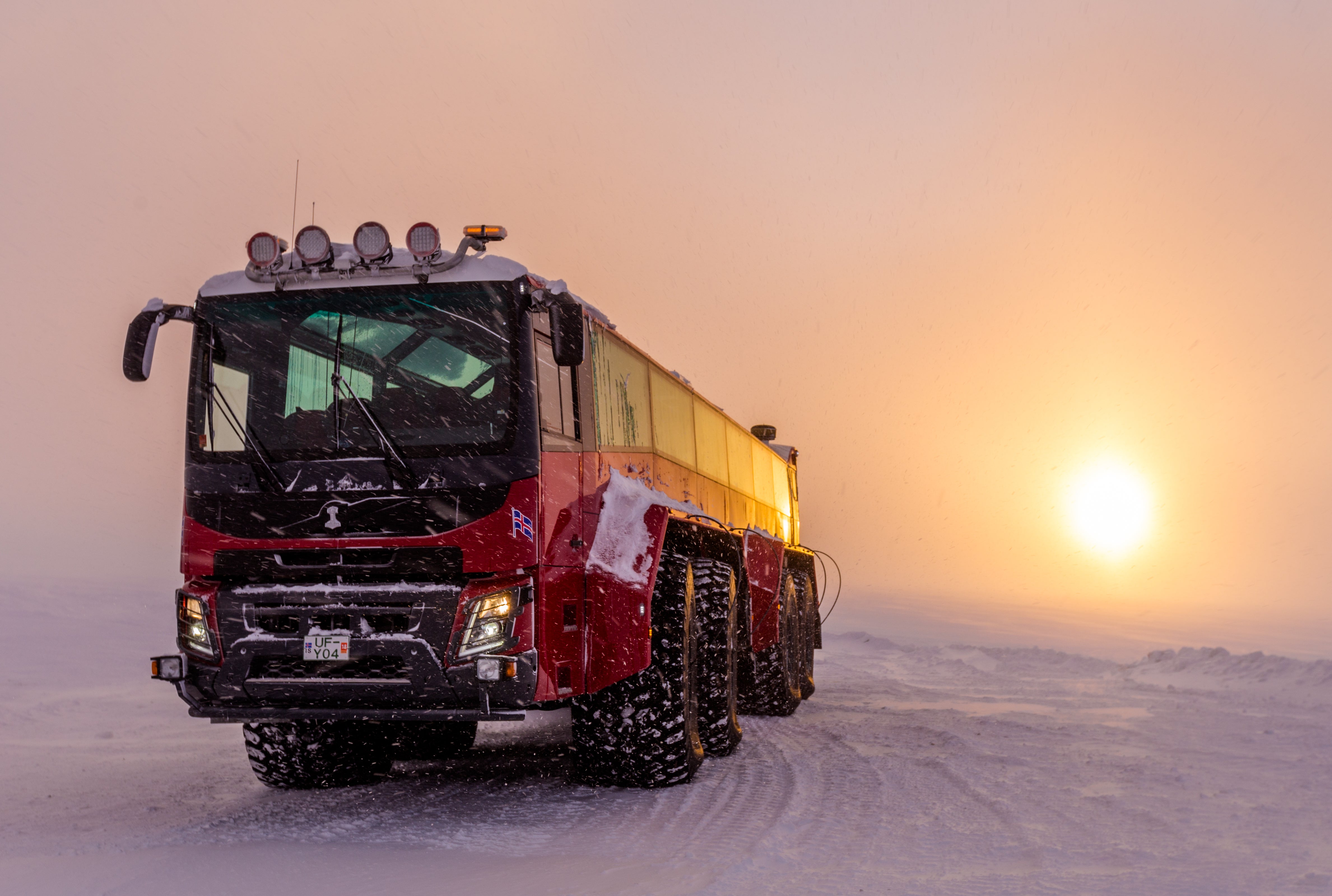 A red monster glacier truck is parked on Langjokull Glacier in Iceland, illuminated by the soft light of the midnight sun.