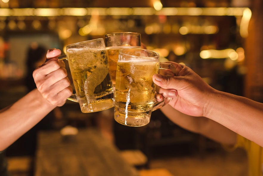 Friends toasting with cold beer mugs at a cozy bar, one of the fun ways to unwind while vacationing in Iceland.