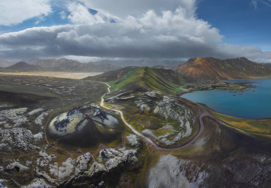 Aerial view of a volcanic crater and coastal road in Iceland, where weather conditions vary by region.