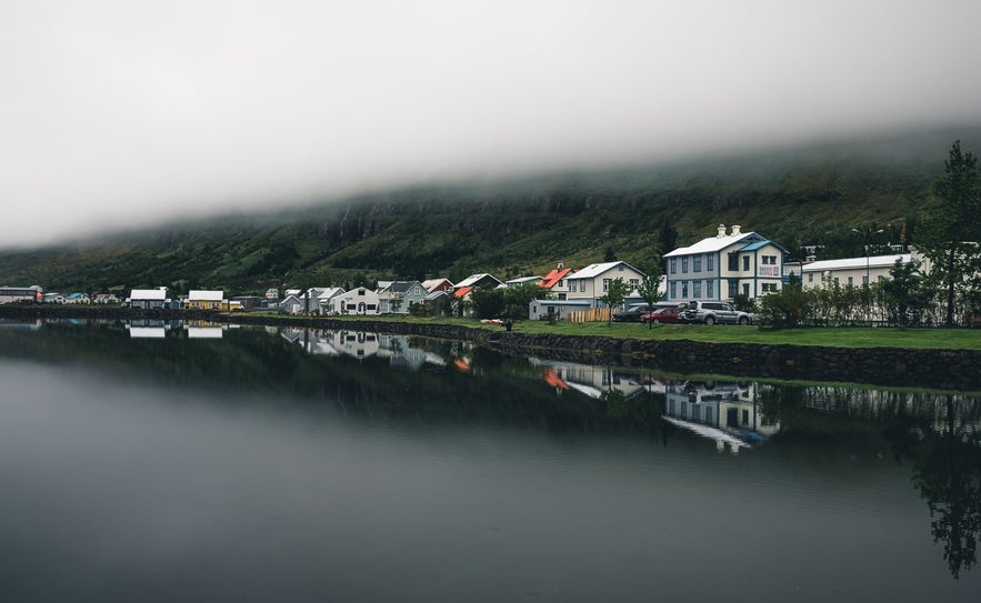 Houses line a still waterfront under low-hanging fog in Iceland.