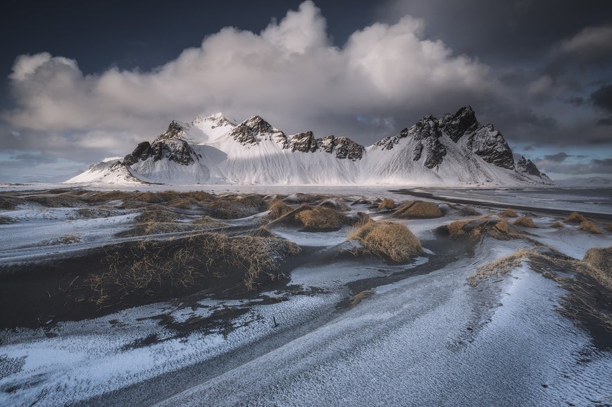 Snow-dusted black sand dunes lead to snow-covered peaks at Vestrahorn in Iceland.