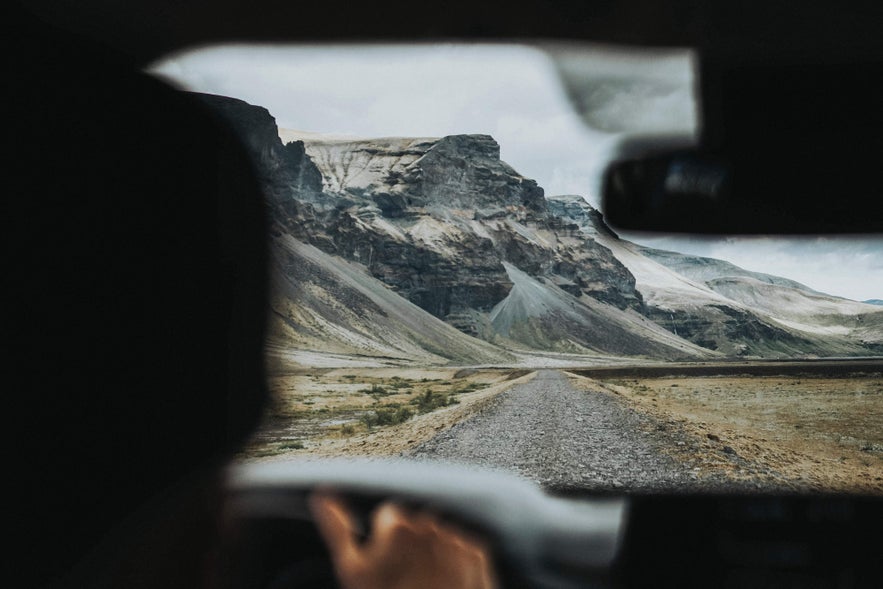 Driving on a remote gravel road toward rugged mountains, perfect for vacationing in Iceland.