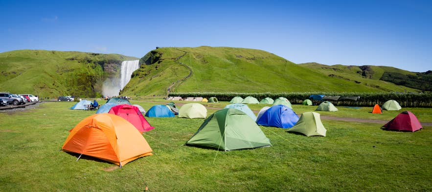 Kolorowe namioty rozstawione w pobliżu wodospadu Skogafoss w słoneczny dzień — jeden z najlepszych sposobów na bliskie poznanie islandzkiej przyrody. 