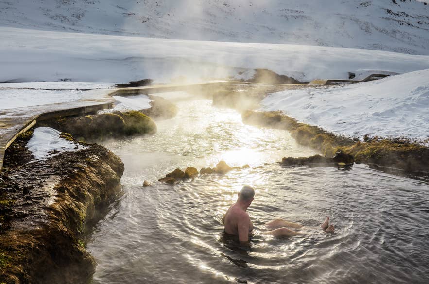 Mężczyzna kąpiący się w parującym gorącym źródle otoczonym śniegiem w dolinie Reykjadalur, popularnym obszarze geotermalnym na Islandii.